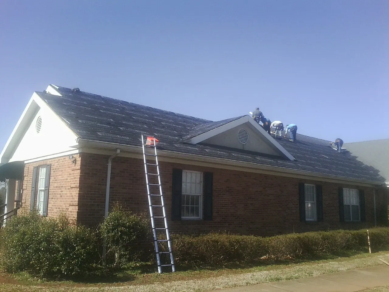 Crew tearing shingles off a brick ranch roof with a ladder set — Metal Roof Repair work by our crew in Pacoima