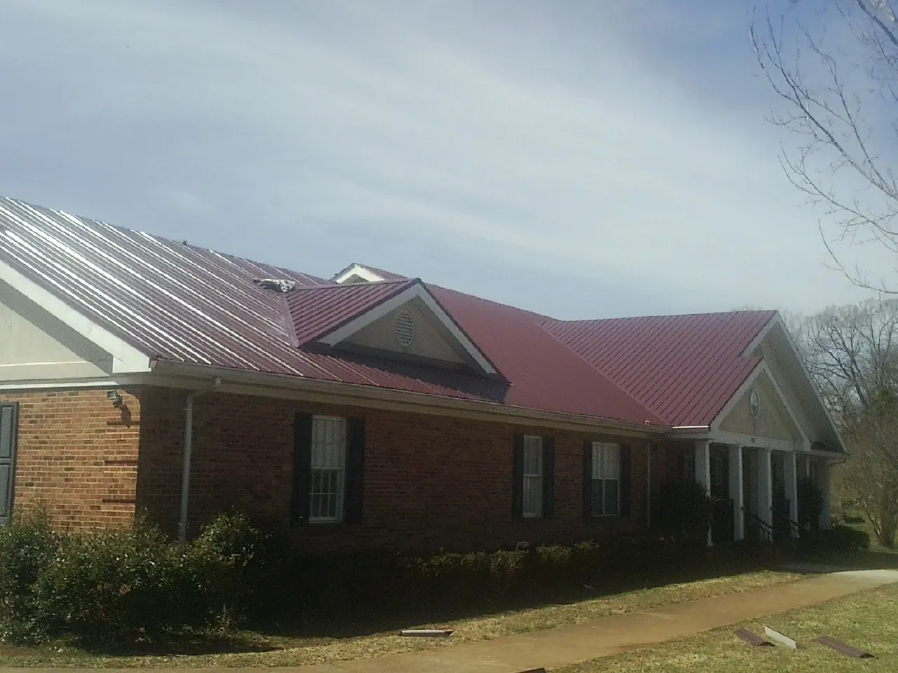 Red metal roof with gabled entries on a long brick building, from a Hail Damage Roof Repair job in Pacoima