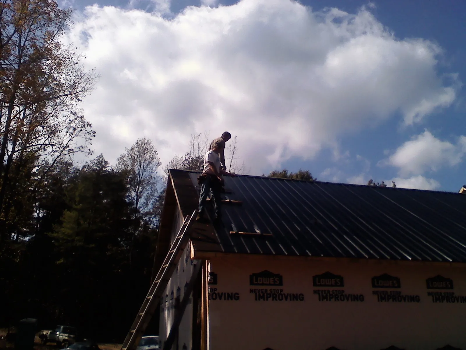 Roofer fastening dark metal panels high against a cloudy sky, from a Roof Inspection job in Pacoima
