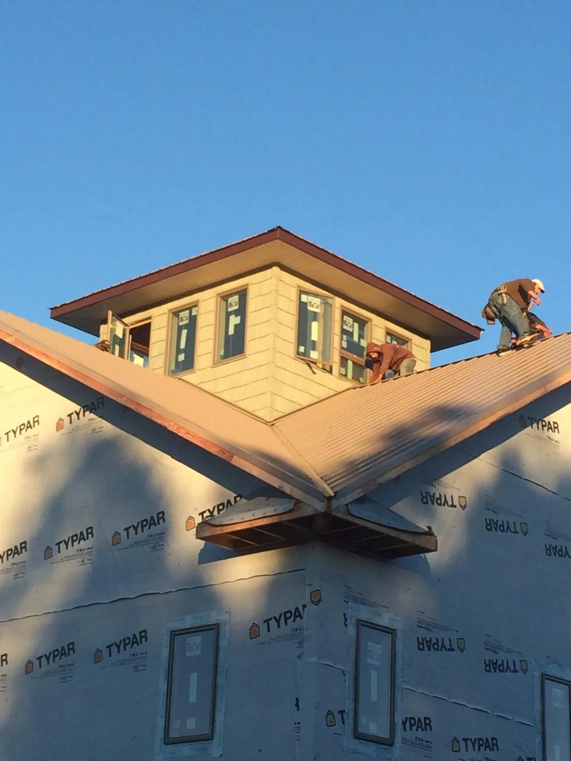 Roofers working around a rooftop cupola on a new metal roof at sunset — Roof Waterproofing in Pacoima by Roofing Brothers
